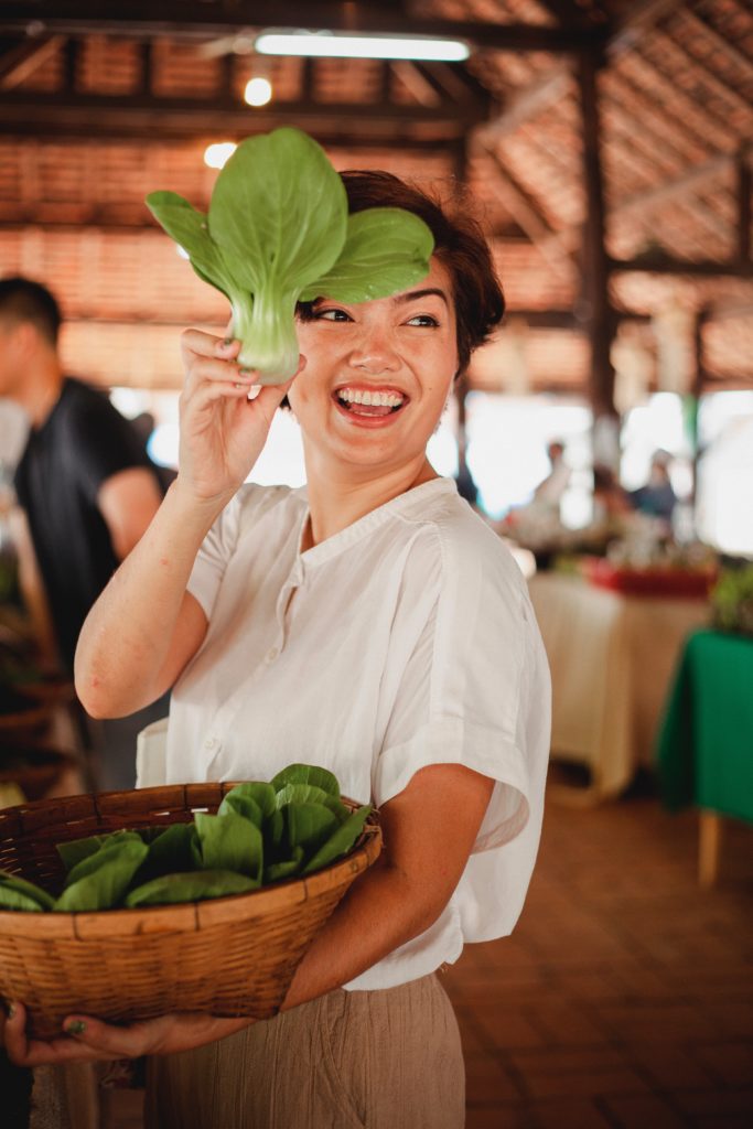 woman holding bok choy, represents a mom starting a cooking business. 